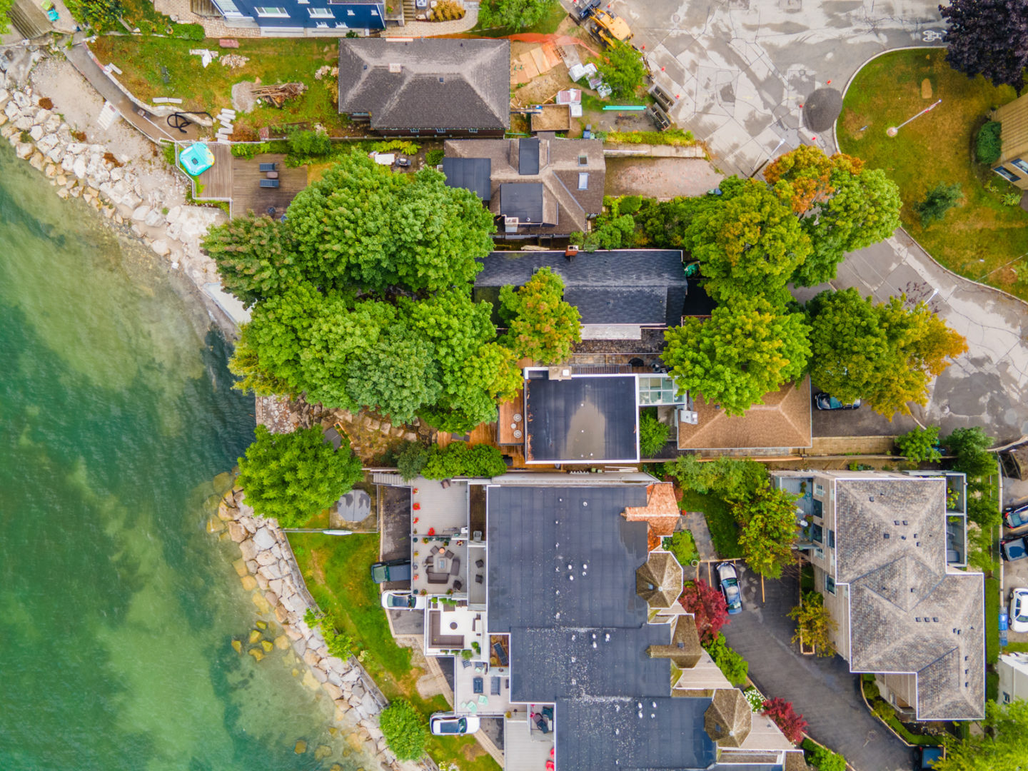 An aerial view of a lakefront residential area, with lots of houses and trees along the water.