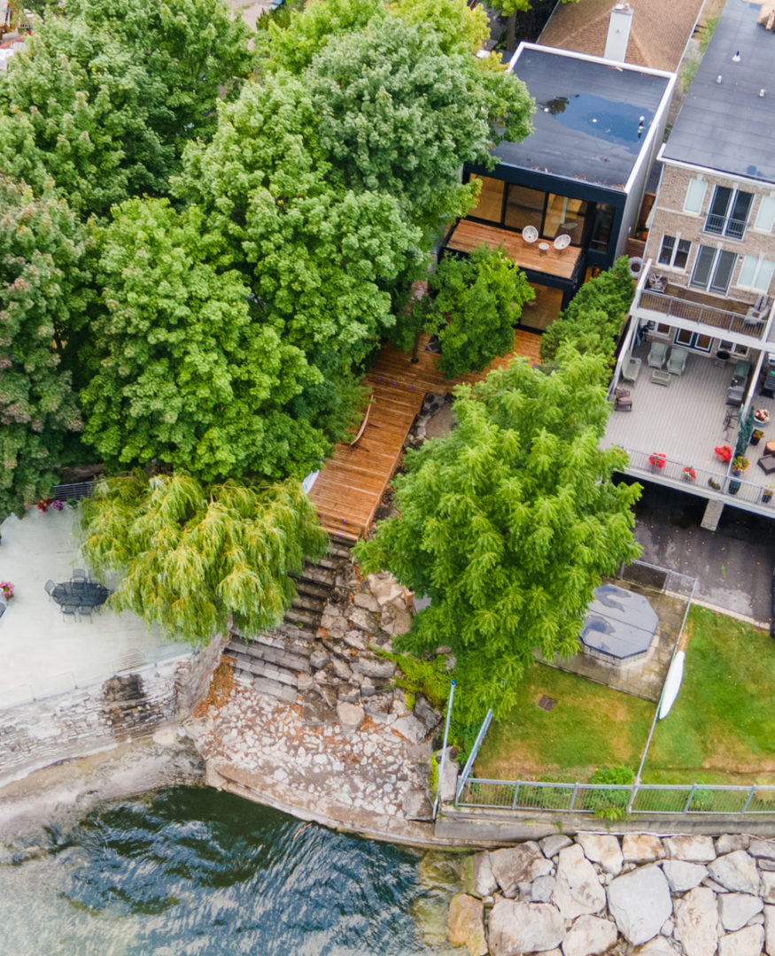 An overhead view of a long but big lakefront property, with a small area of shoreline and a big deck off the back of the house.