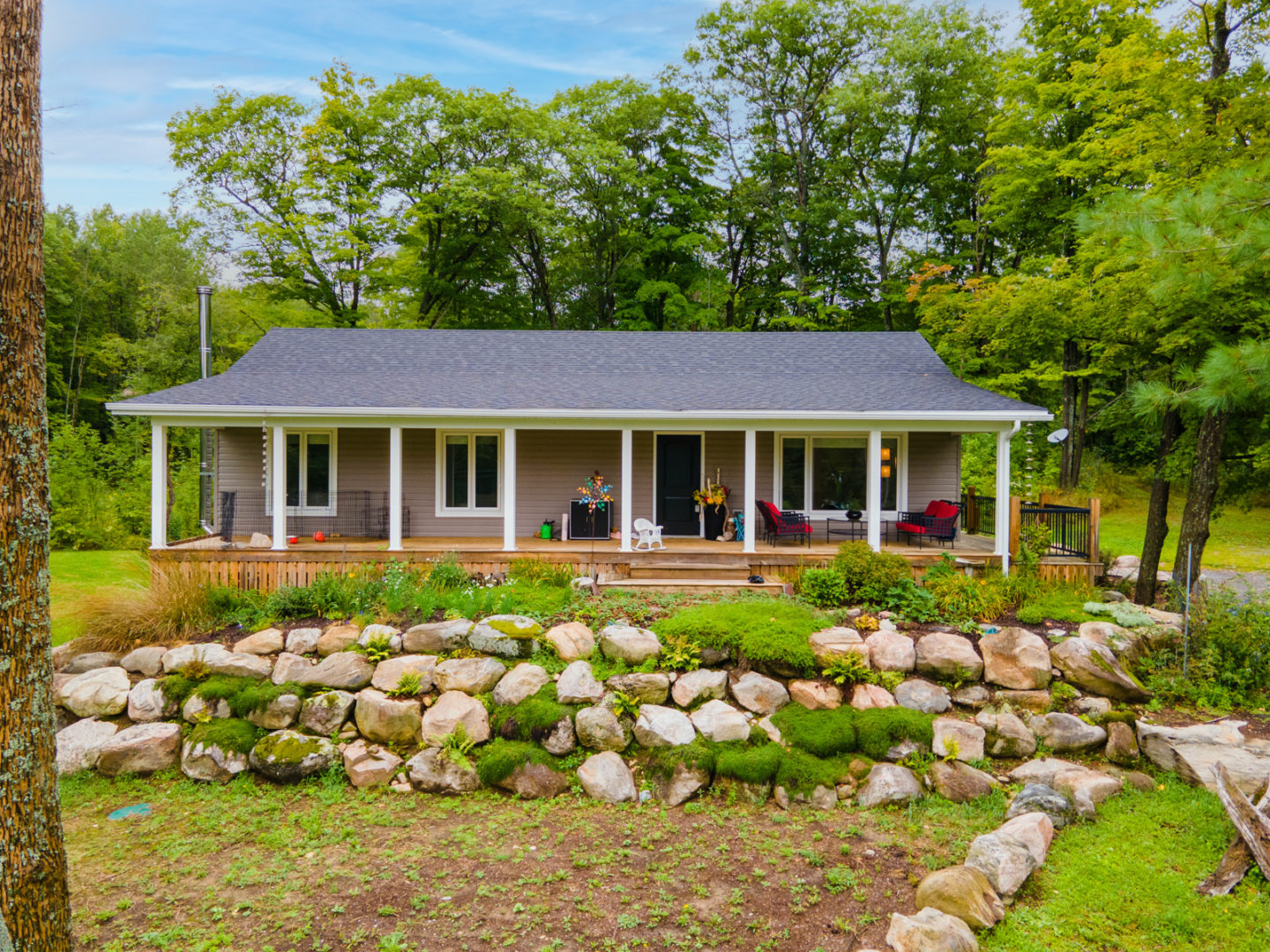 Exterior view of a one-story cottage with large front windows and a front deck spanning the house.