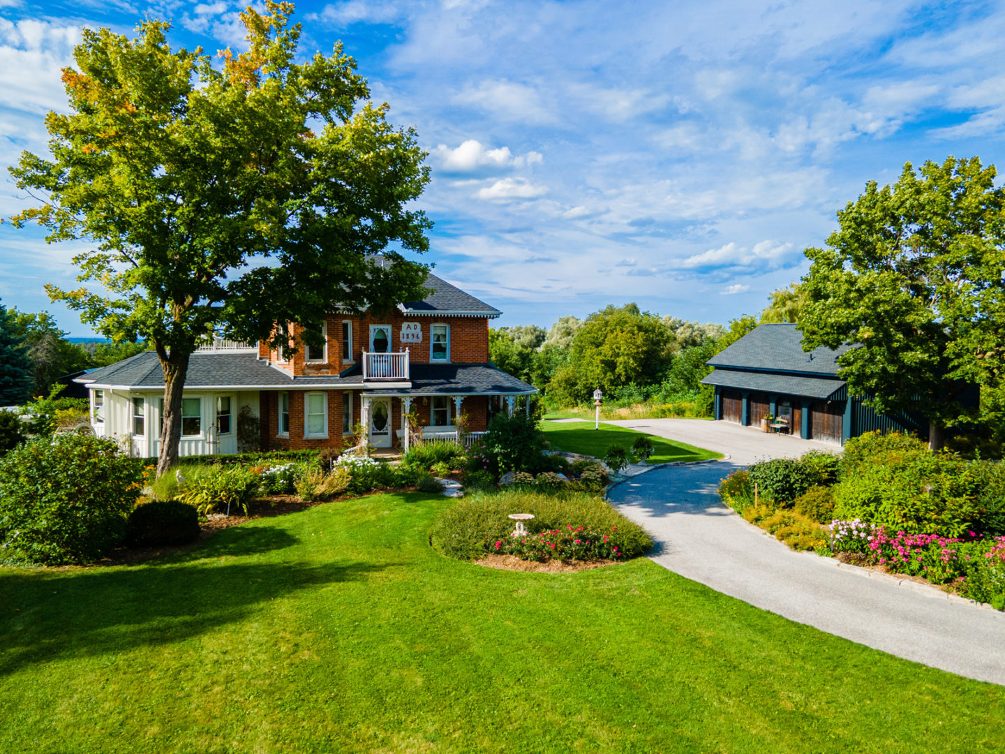 A large, perfectly mowed, green lawn, with a long driveway leading towards a big country home.