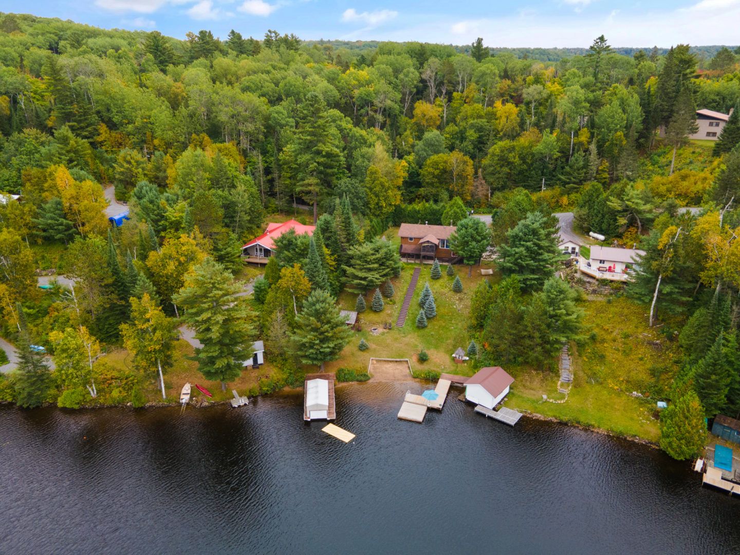 Overhead view of a small section of lake, with a few large homes set back from the shoreline and trees in behind them.