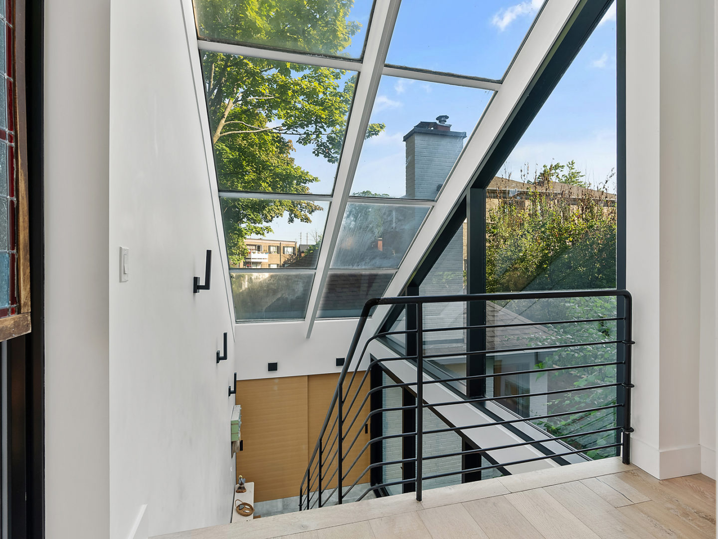 A bright stairway landing with a black metal railing, looking out to a glass ceiling and a wall of windows.