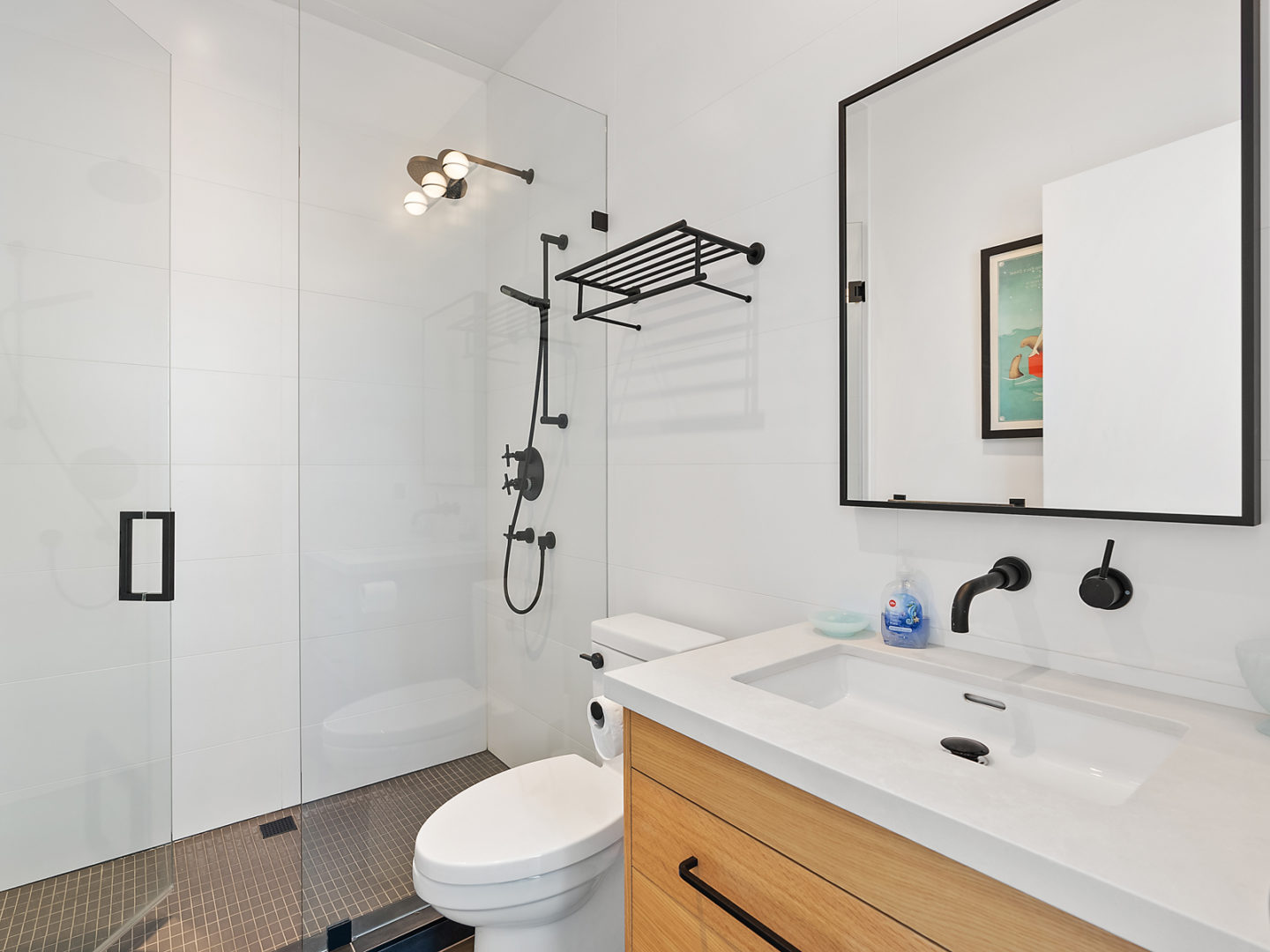 A simple bathroom with white and light wood accents, with a toilet, a shower and a sink..