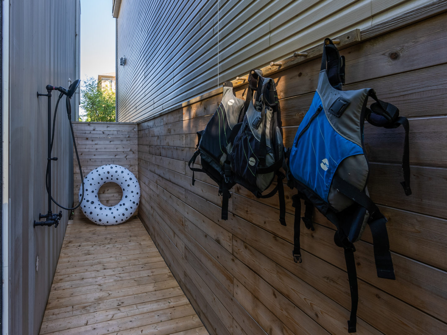 A narrow outdoor space with wood-panelled walls and decking that has an outdoor shower and a place to hang lifejackets.