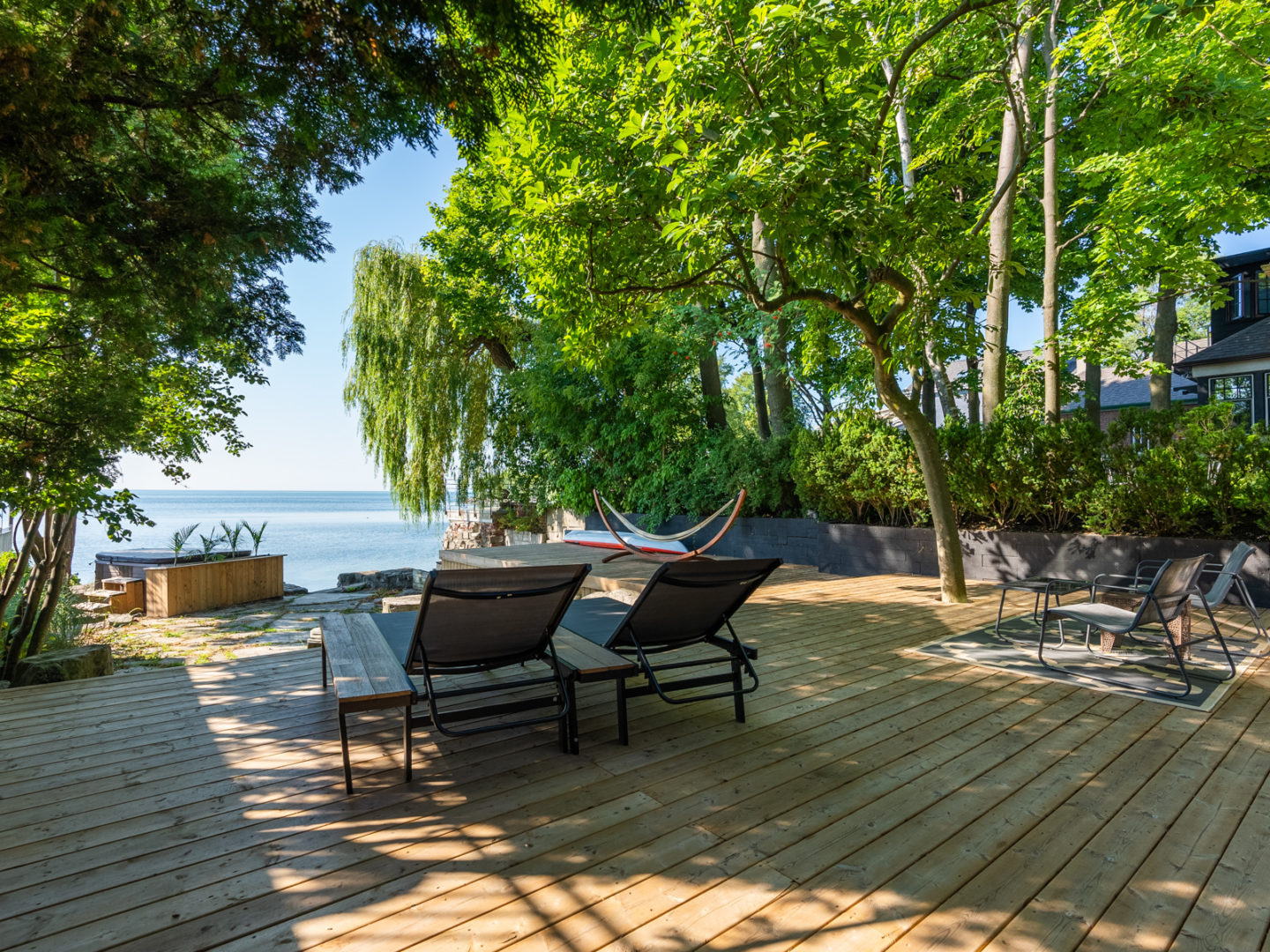 An outdoor wooden deck with recliner chairs, surrounded by trees and looking out over a lake.