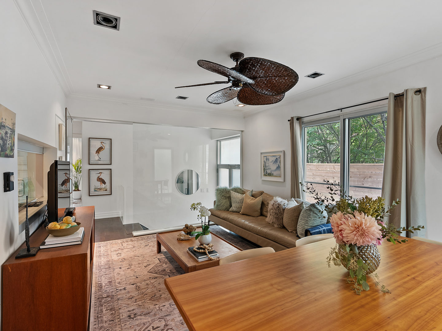 A small but bright living space with a dining table and a couch, with floor-to-ceiling windows along one wall.