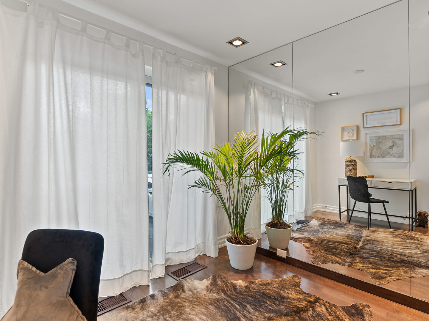 A roomy office area with a little desk, a chair, large windows, and an indoor palm plant in one corner.