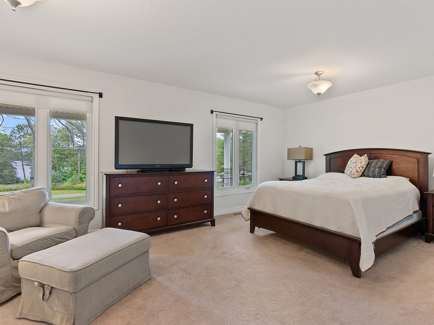 A large bedroom with a big bed, a chair, a television, and two large windows.