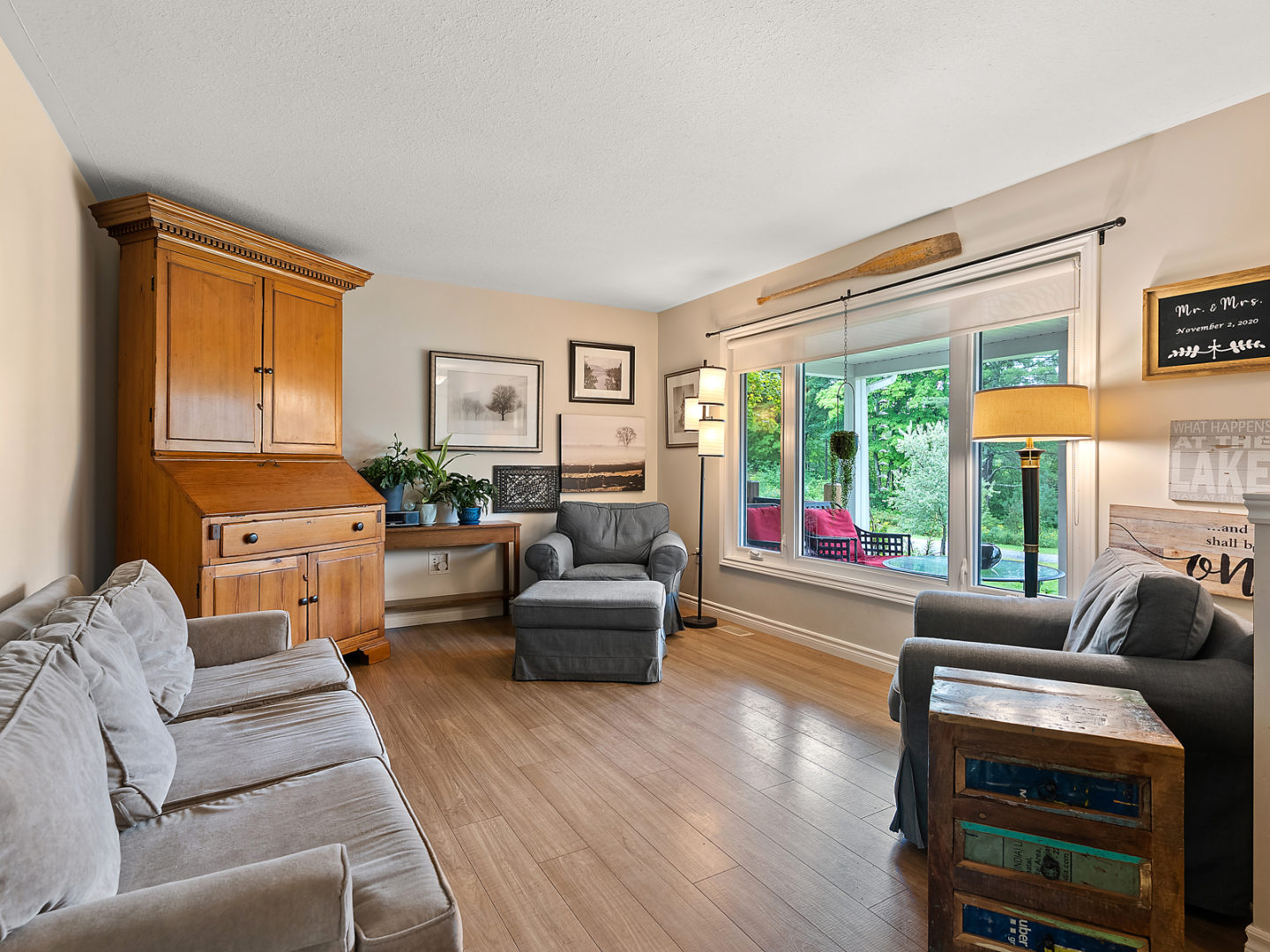 A large bright living room with a big front window, hardwood floors, and a couch and two chairs.