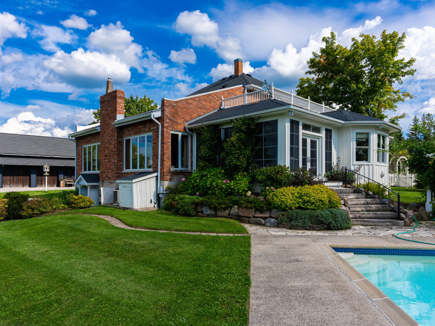 The back of a large house, with a sunroom that walks out to an outdoor pool area.