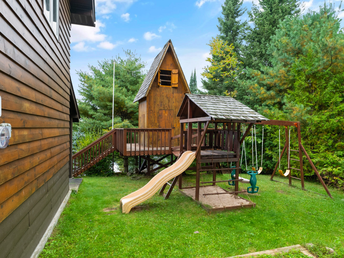 An outdoor children's play structure with a slide, swings, deck, and playhouse.