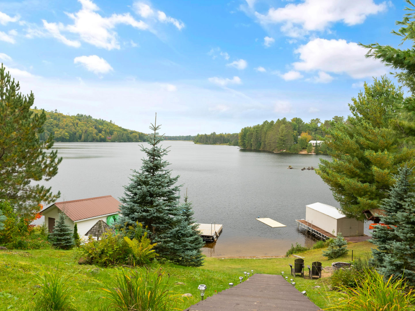 Stairs leading down to a lakefront area that has a long dock and a small sandy beach.