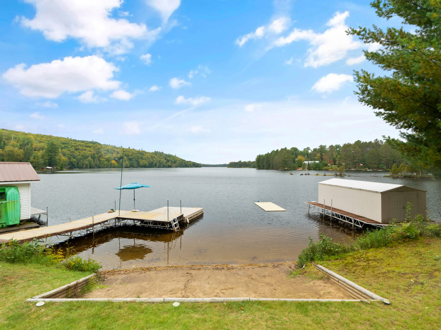 A small sandy beach on a lake, surrounded by grass, with a long dock beside it.