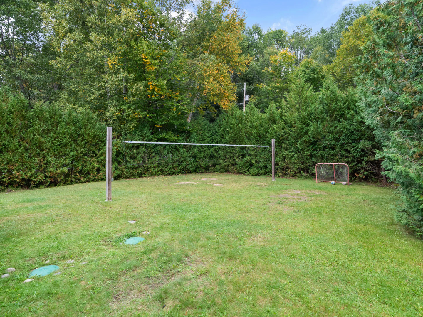 A grassy outdoor space surrounded by trees with a volleyball net in the middle.