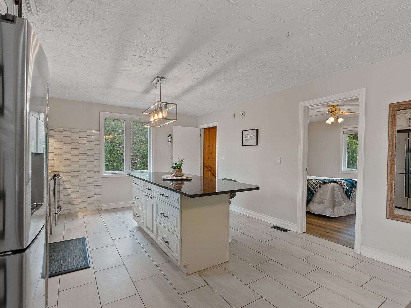 A bright, roomy kitchen area with an island, and a bedroom branching off to the side through a doorway.