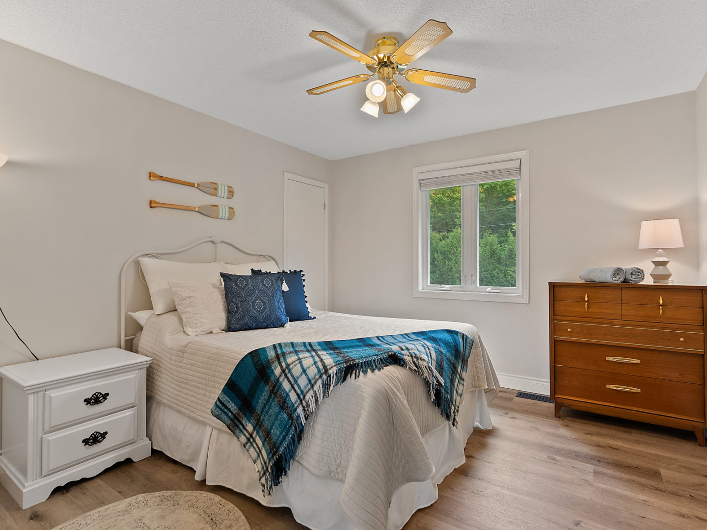 A bright bedroom with a large bed, wood floors, and decorative canoe paddles on the wall above the bed.