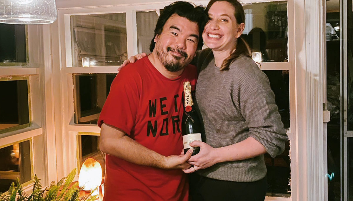 couple Jen Pogue and Warren Sonoda stand together in the sunroom at the their cottage