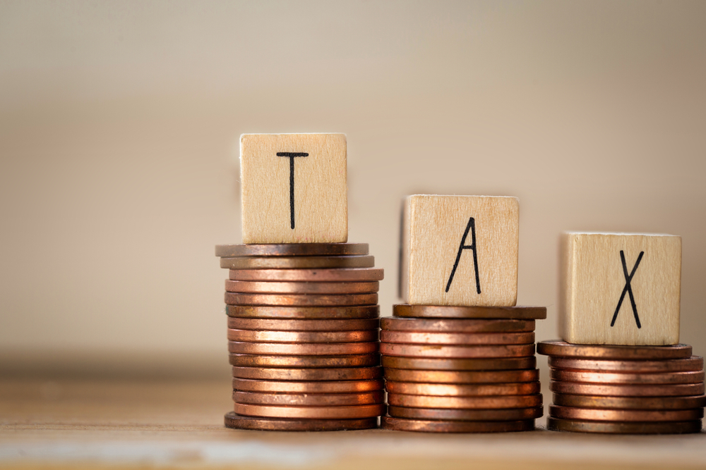 The word TAX spelled out in wooden cubes, stacked on coins