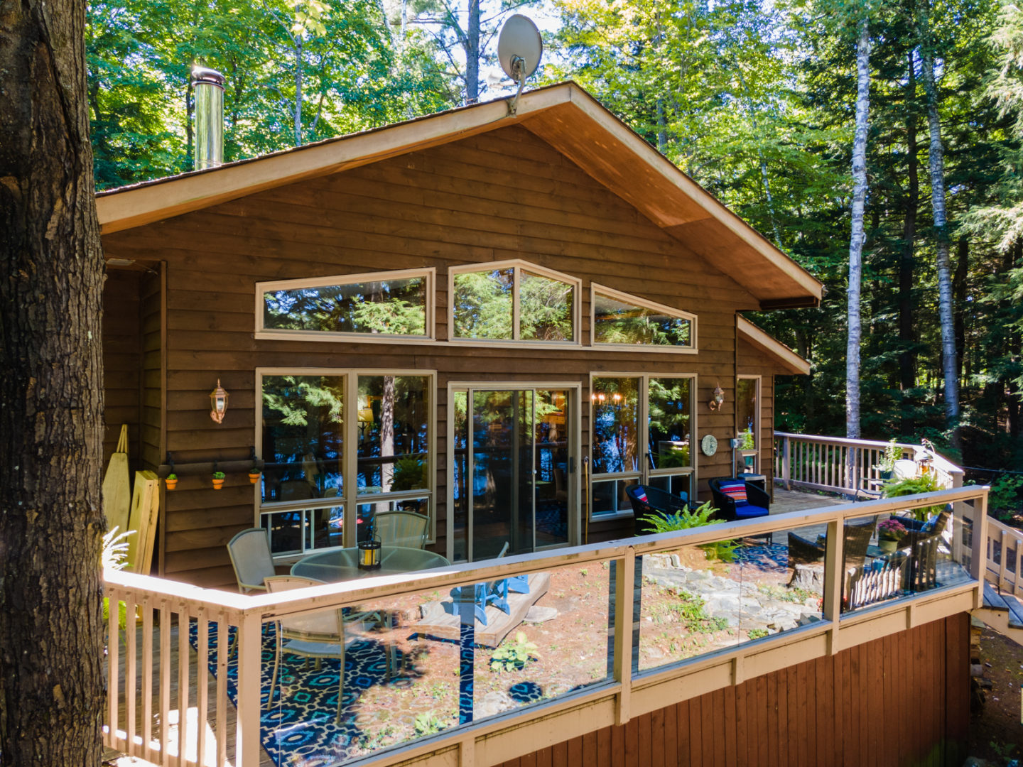 A wood frame cottage with huge windows and a large deck.