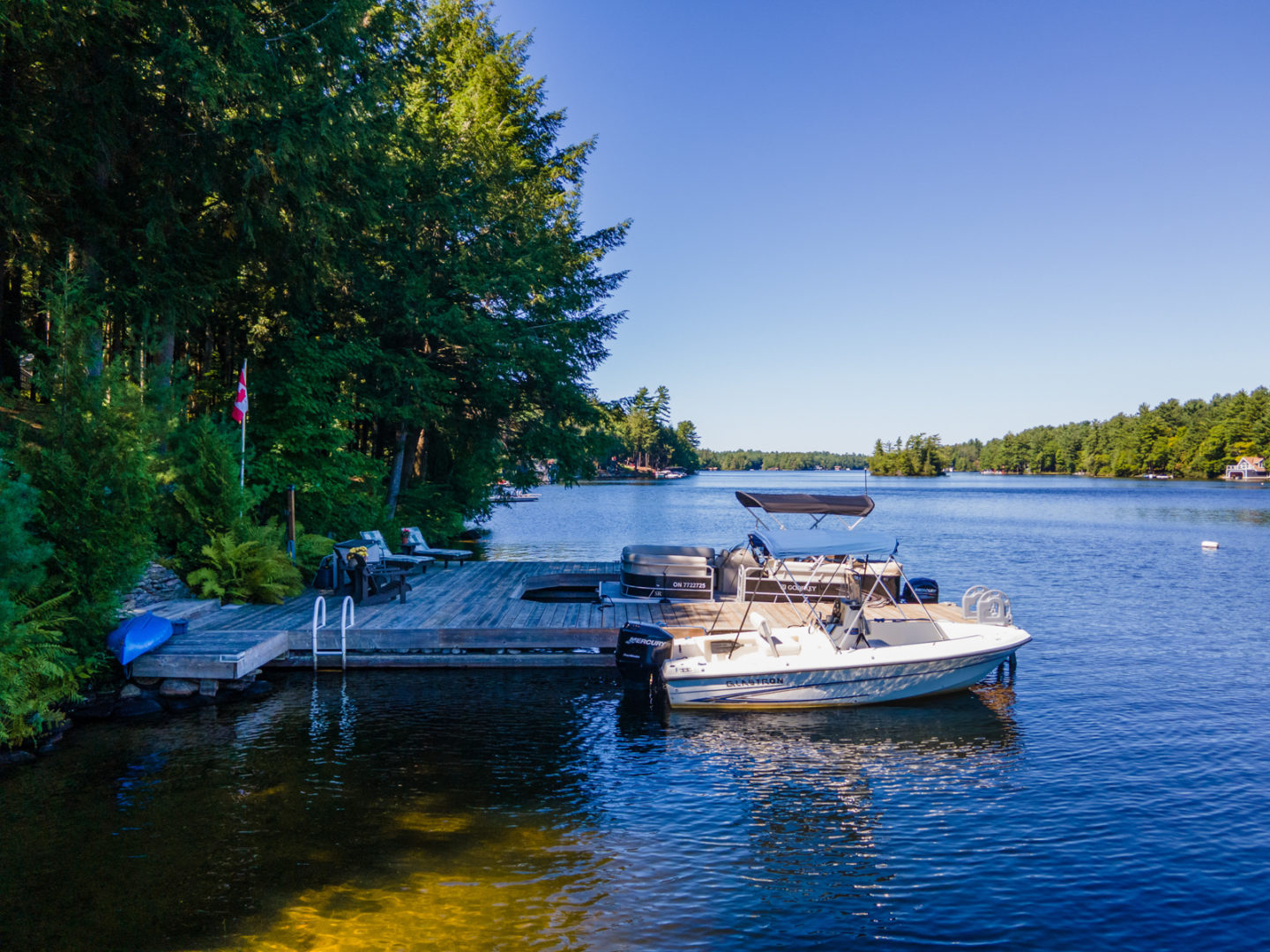 A small boat sits anchored to a dock on a peaceful stretch of blue lake.