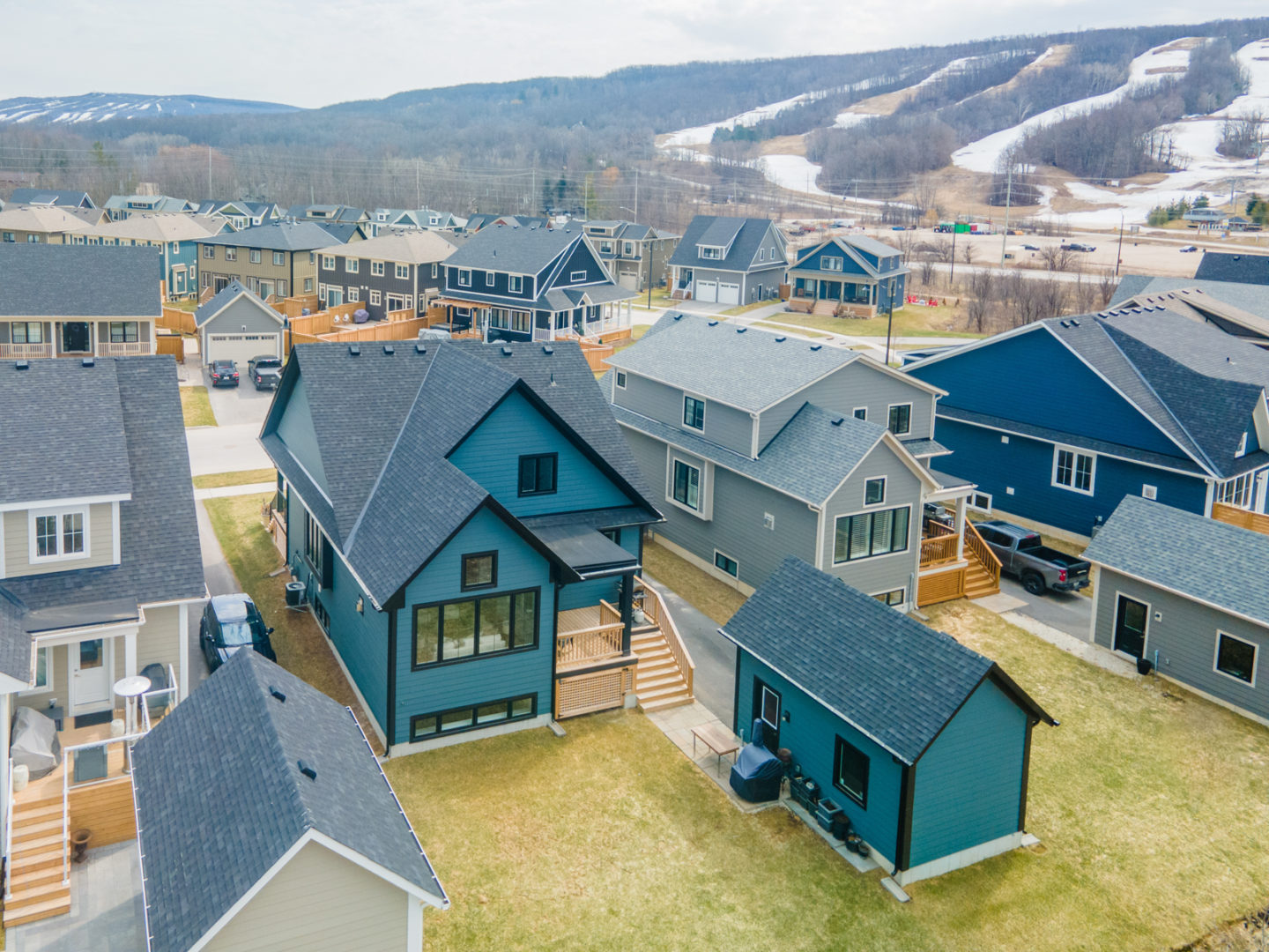Overhead view of the backyard of a house on a residential street. The two-story house has a dark blue exterior and a matching detached single car garage extending into the backyard area.
