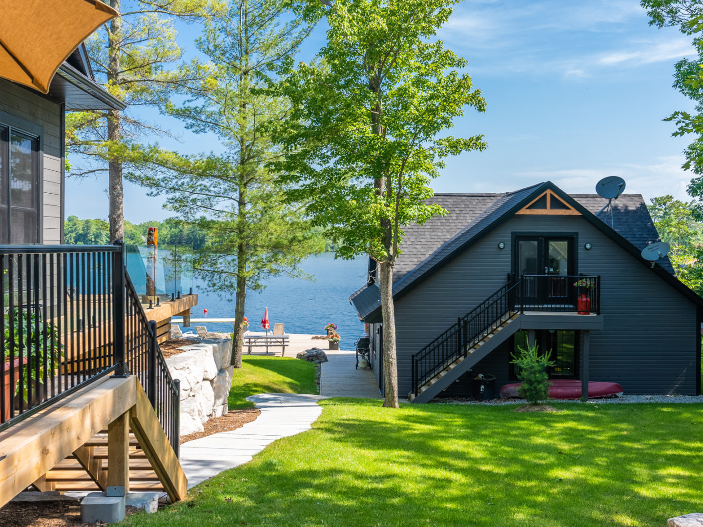 The side of a cottage with stairs leading down to the waterfront area, which has a big boathouse and a large dock.