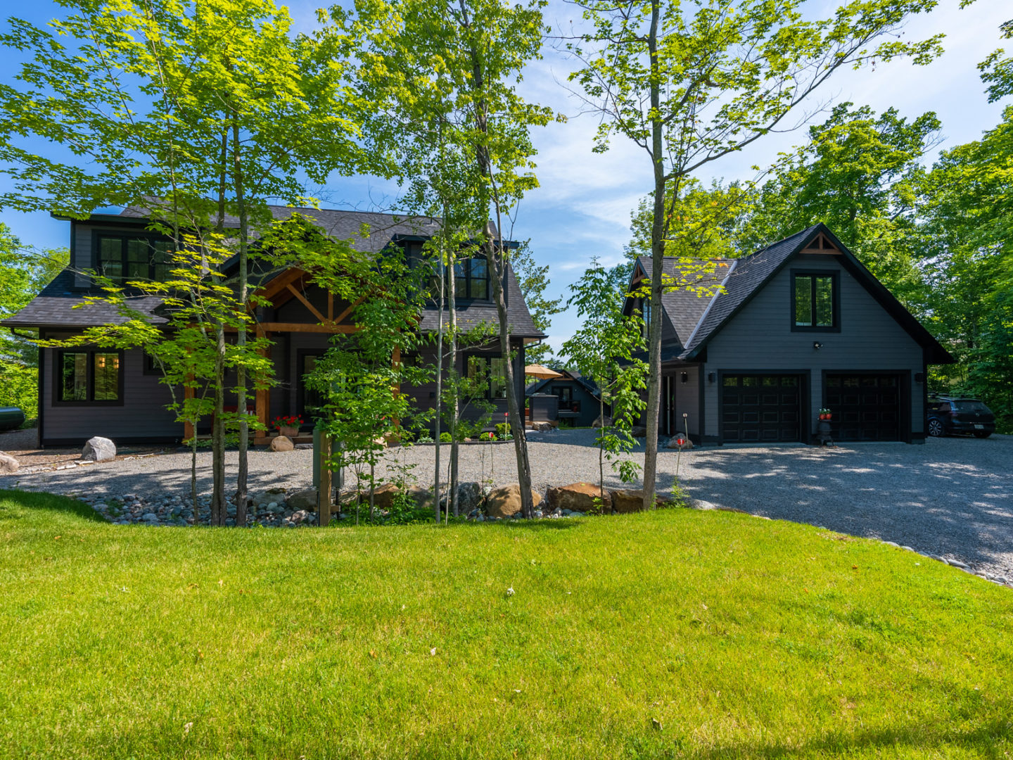 A grassy space in front of a paved area leading to a cottage and an adjacent detached garage.