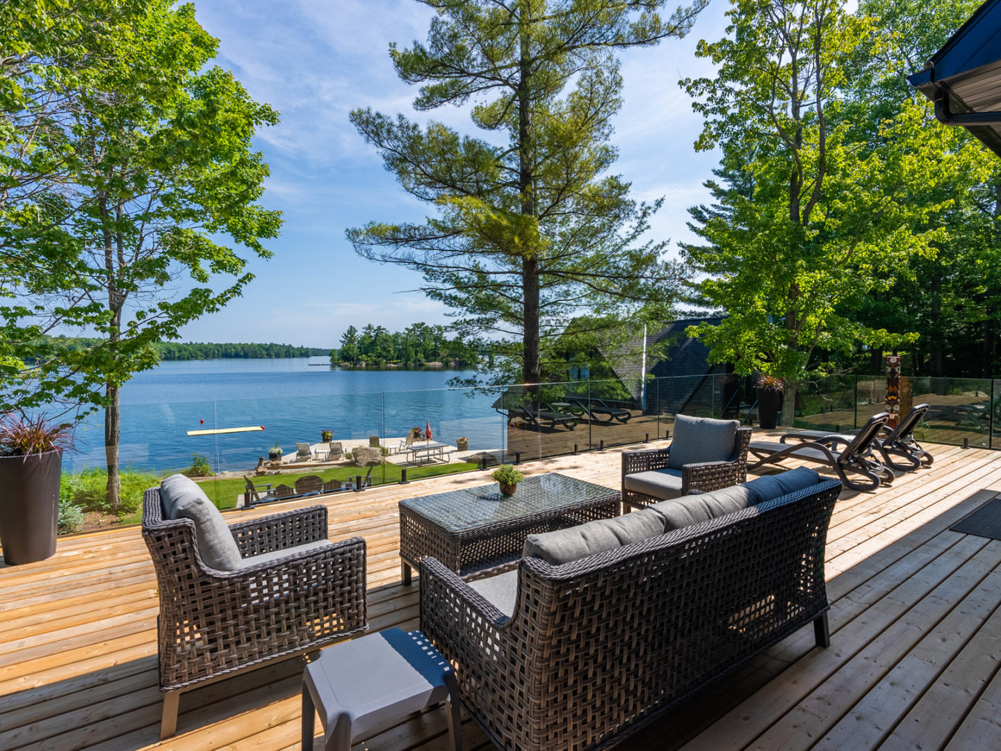 A large deck facing a lake with outdoor patio furniture and a glass railing.
