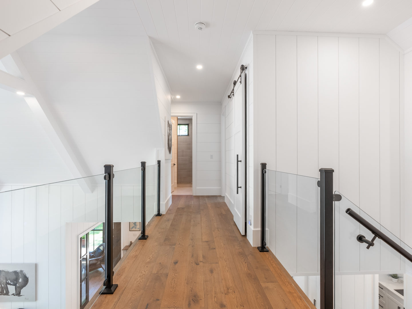 A second-story hallway with wooden floors and glass railings.