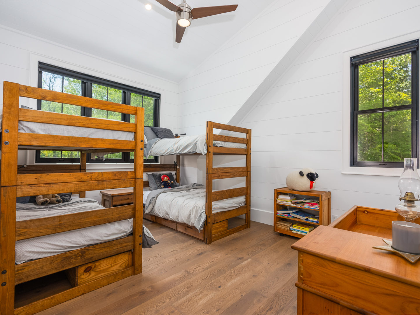A spacious bedroom with two sets of bunkbeds, white walls, and wooden floors.