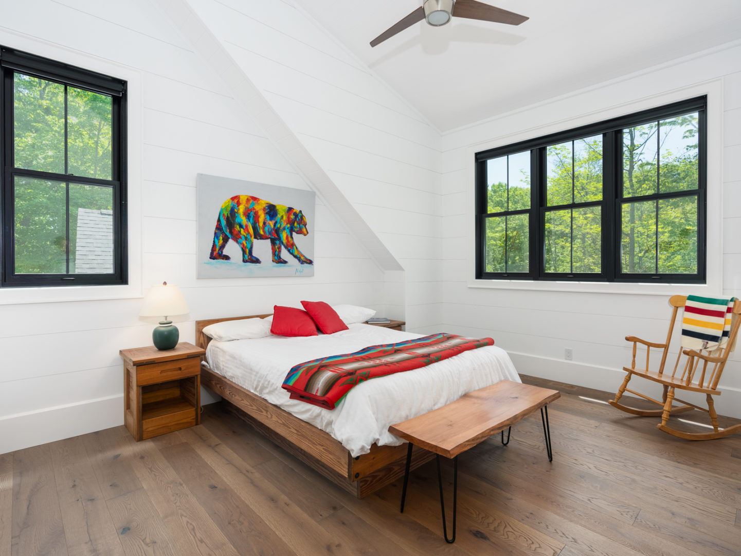 A bedroom with a large window, dark wooden floors, and white walls.