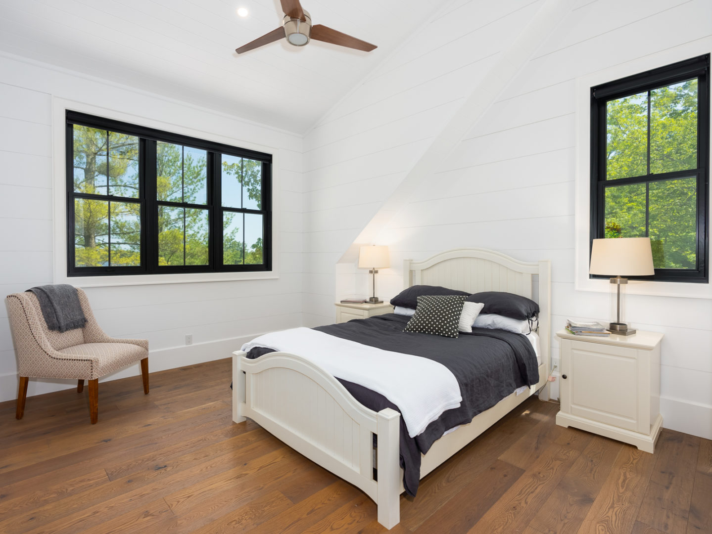 A bedroom with a large window, dark wooden floors, and white walls.