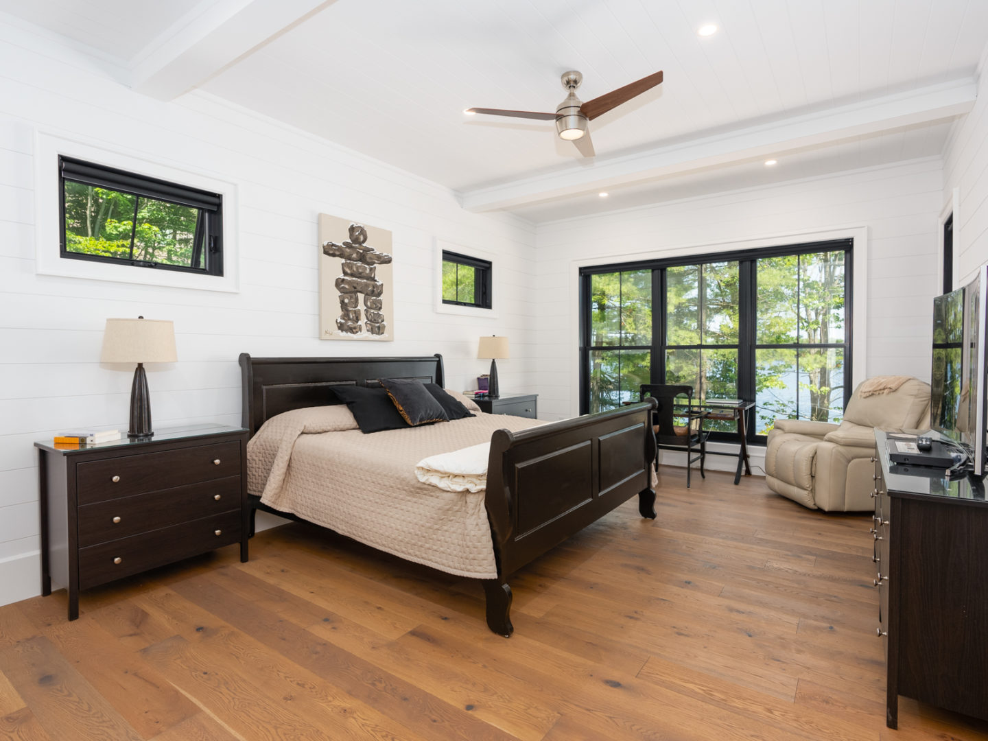 A big bedroom with large windows, hardwood floors, white walls, and a ceiling fan.