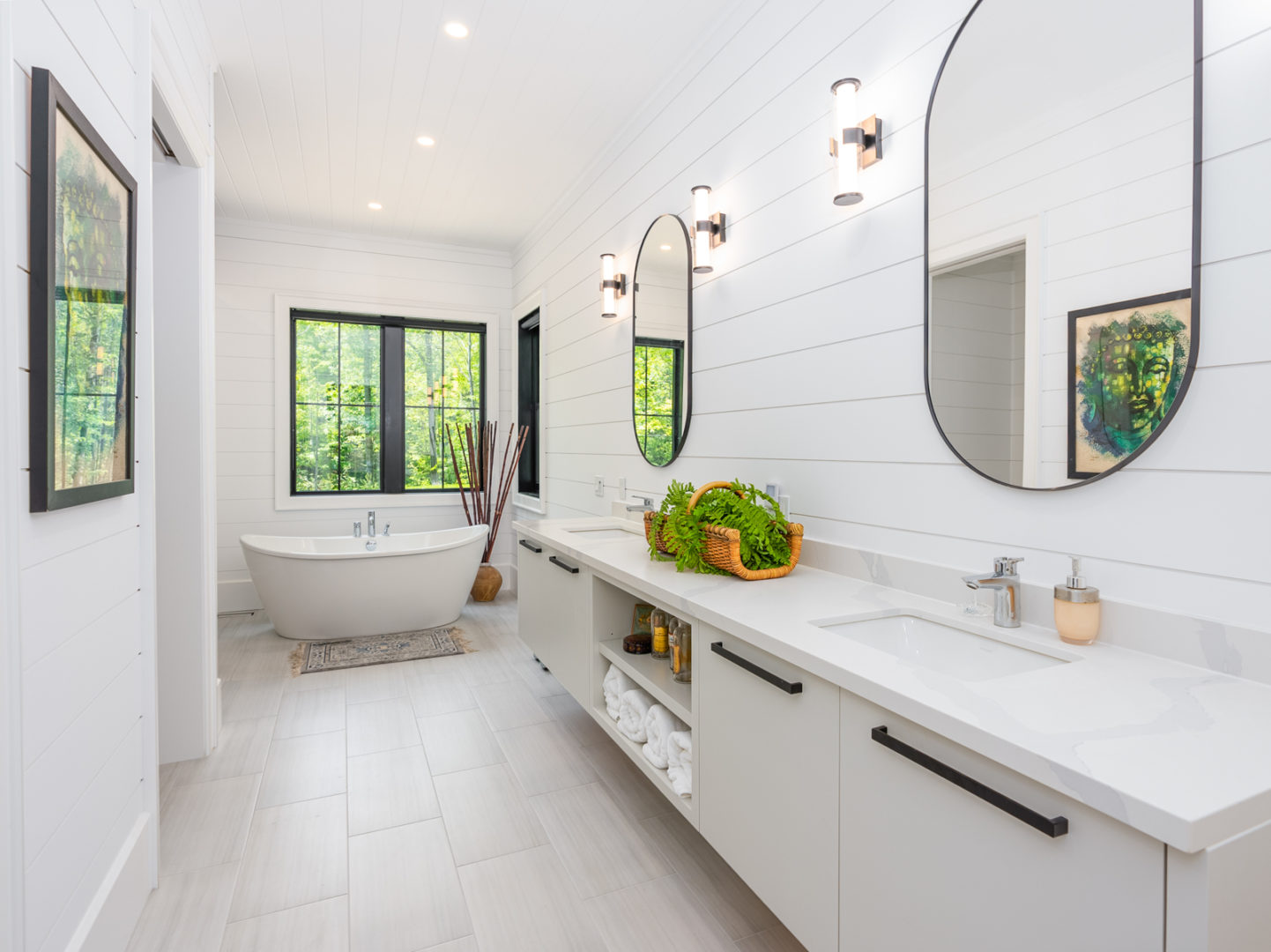 A big ensuite bathroom with a long countertop, double sinks, and a standalone bathtub in front of a big window.