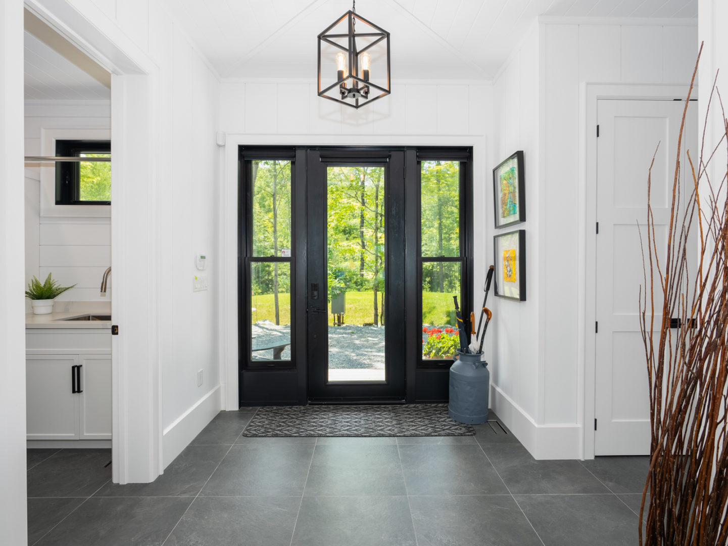 A large, bright entrance of a modern cottage, with white walls, dark floors, and a bathroom off to one side.