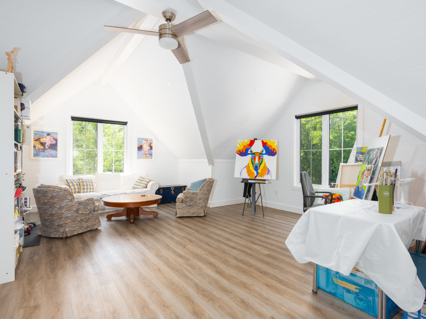 A large, bright living area with sloping ceilings, hardwood floors, and a small sitting area.