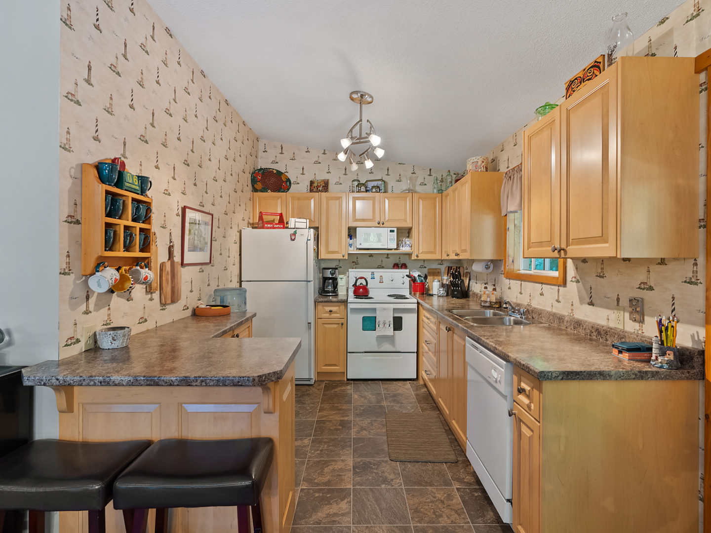A modest kitchen with light wooden cabinets and lighthouse wallpaper on one side.