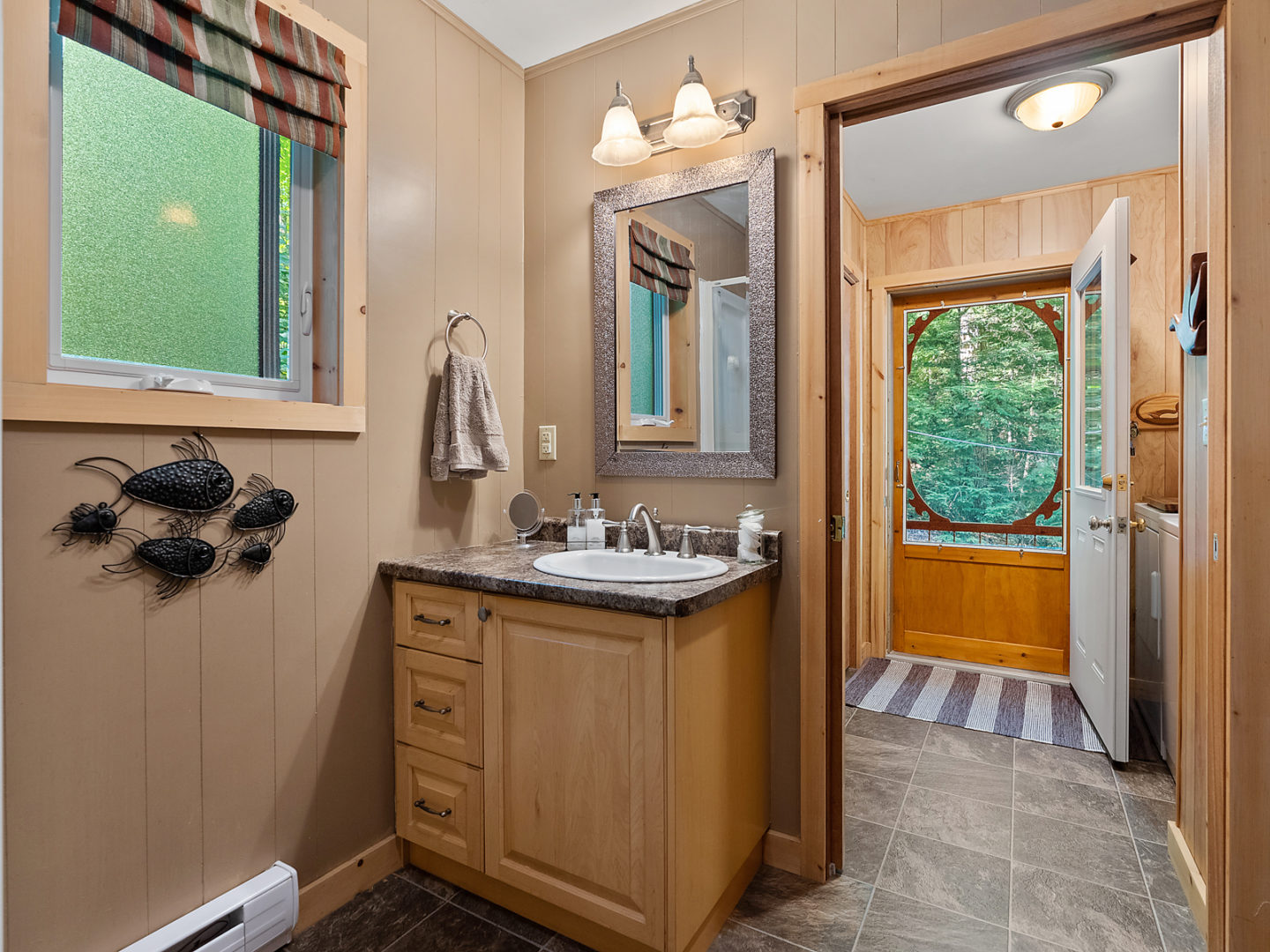 A bathroom with a sink. An open door looks out to an entrance area of a cottage.