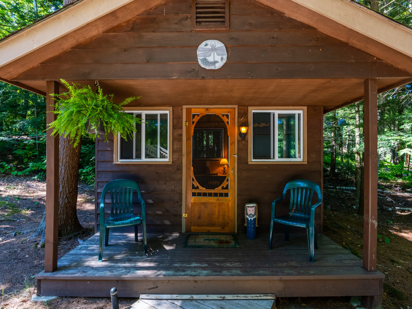 Exterior view of a small wooden bunkie that has two windows on either wide of a screen door.