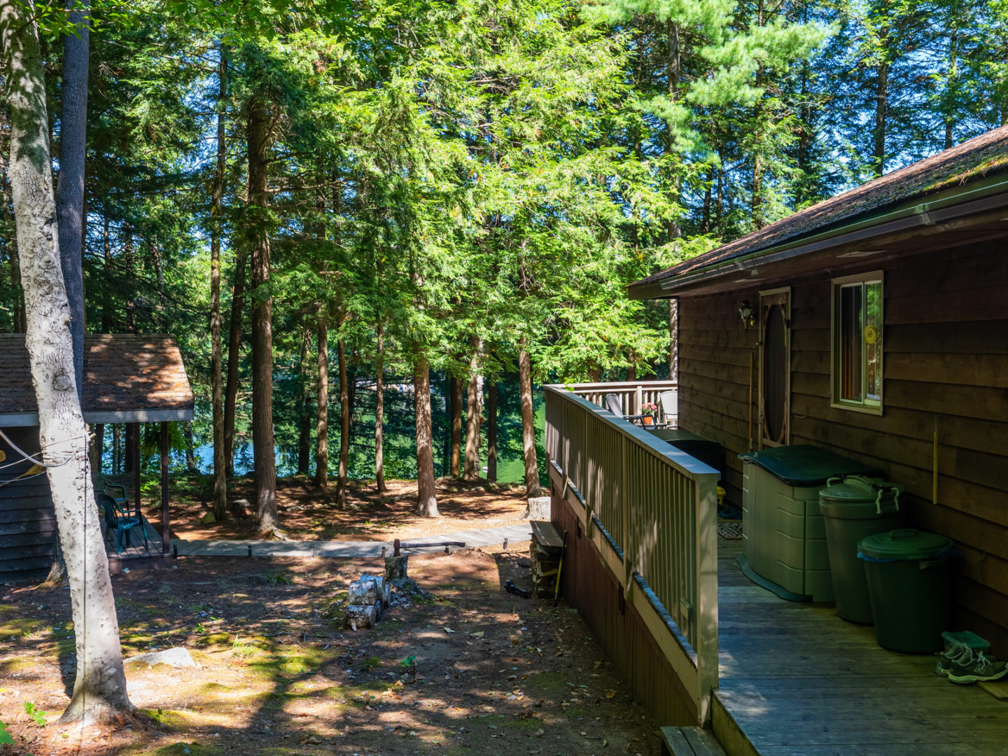 The side of a cottage with a long deck stretching down its length. To the left of the cottage is a small bunkie.