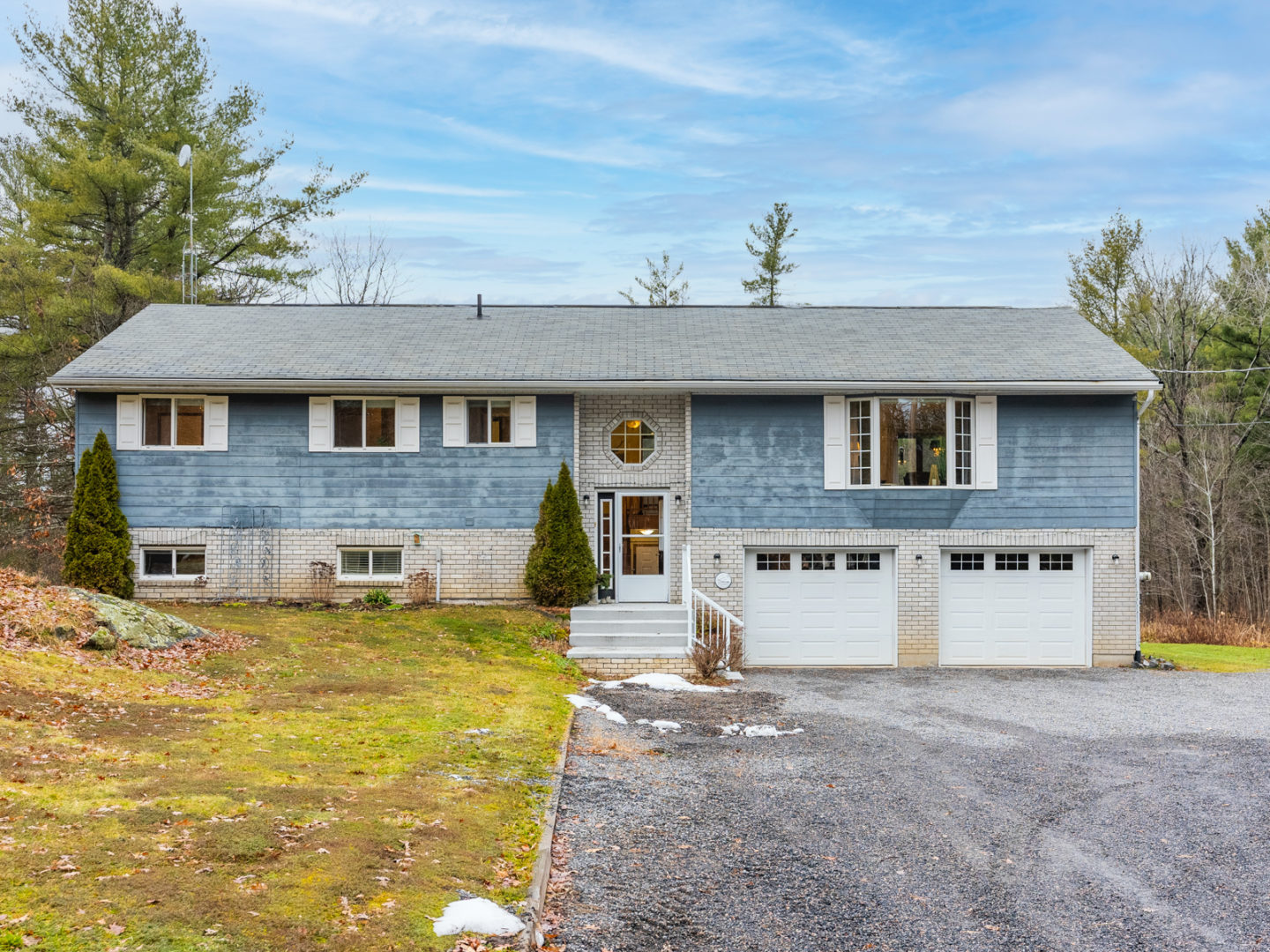 The front of a raised bungalow that has a light blue exterior and white garage doors.