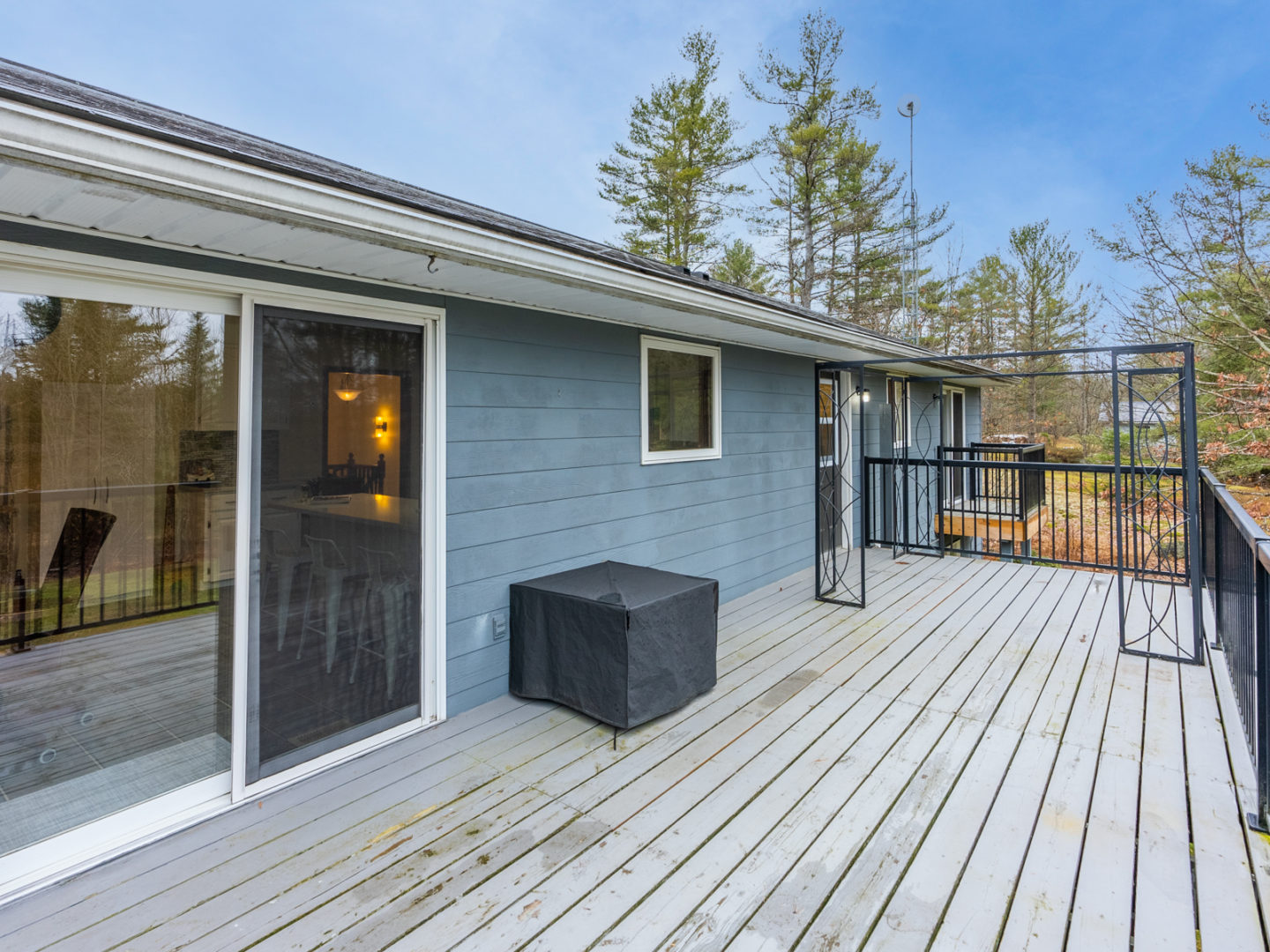 A large deck off the back of a baby blue home, with sliding double doors leading into a kitchen.