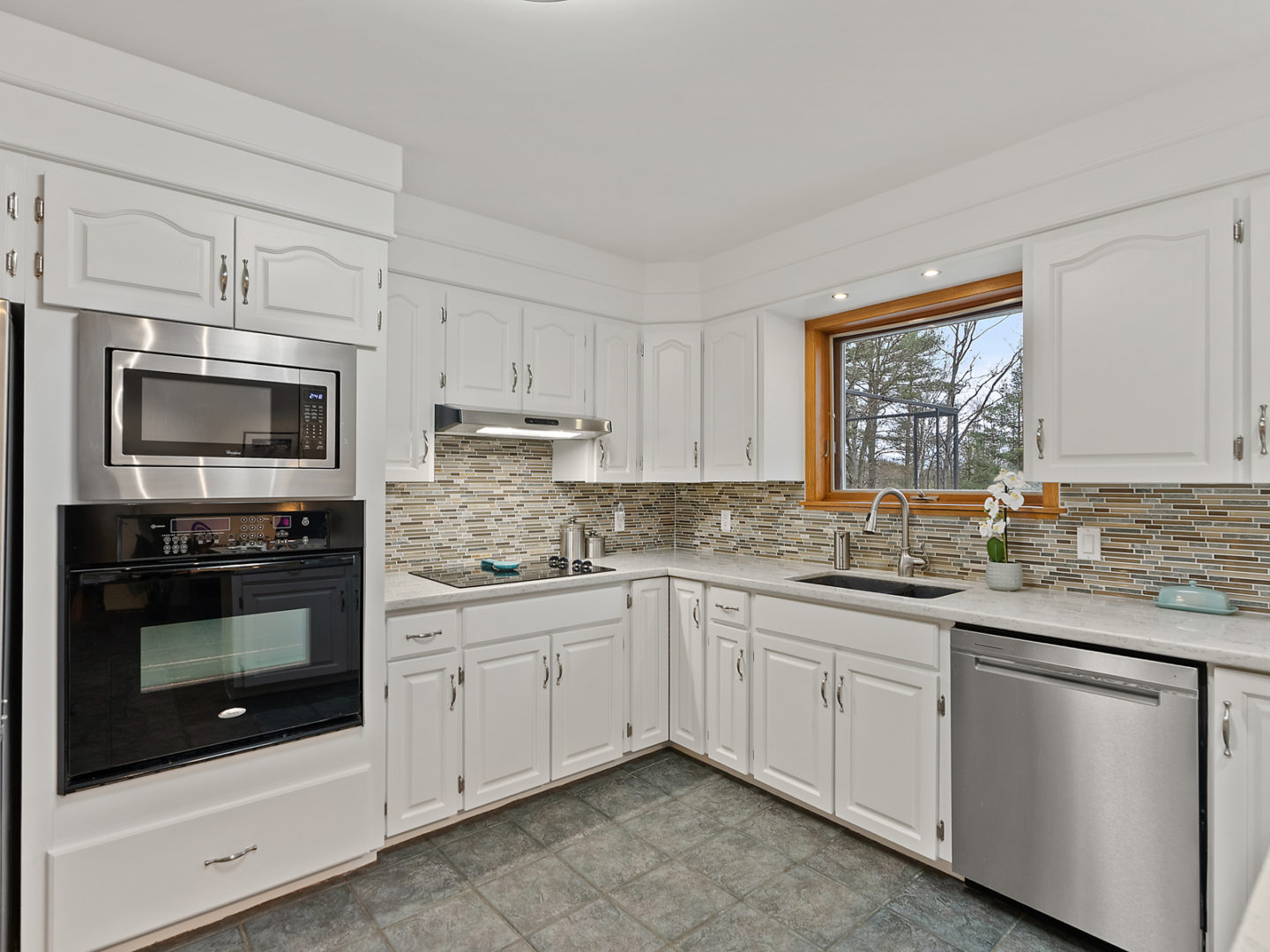 A big kitchen area with tile flooring, white cupboards, and updated appliances.