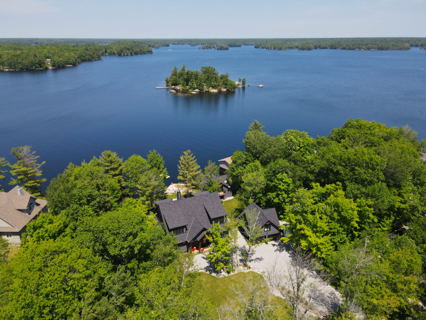An overhead view of a large lakefront cottage, surrounded by trees.