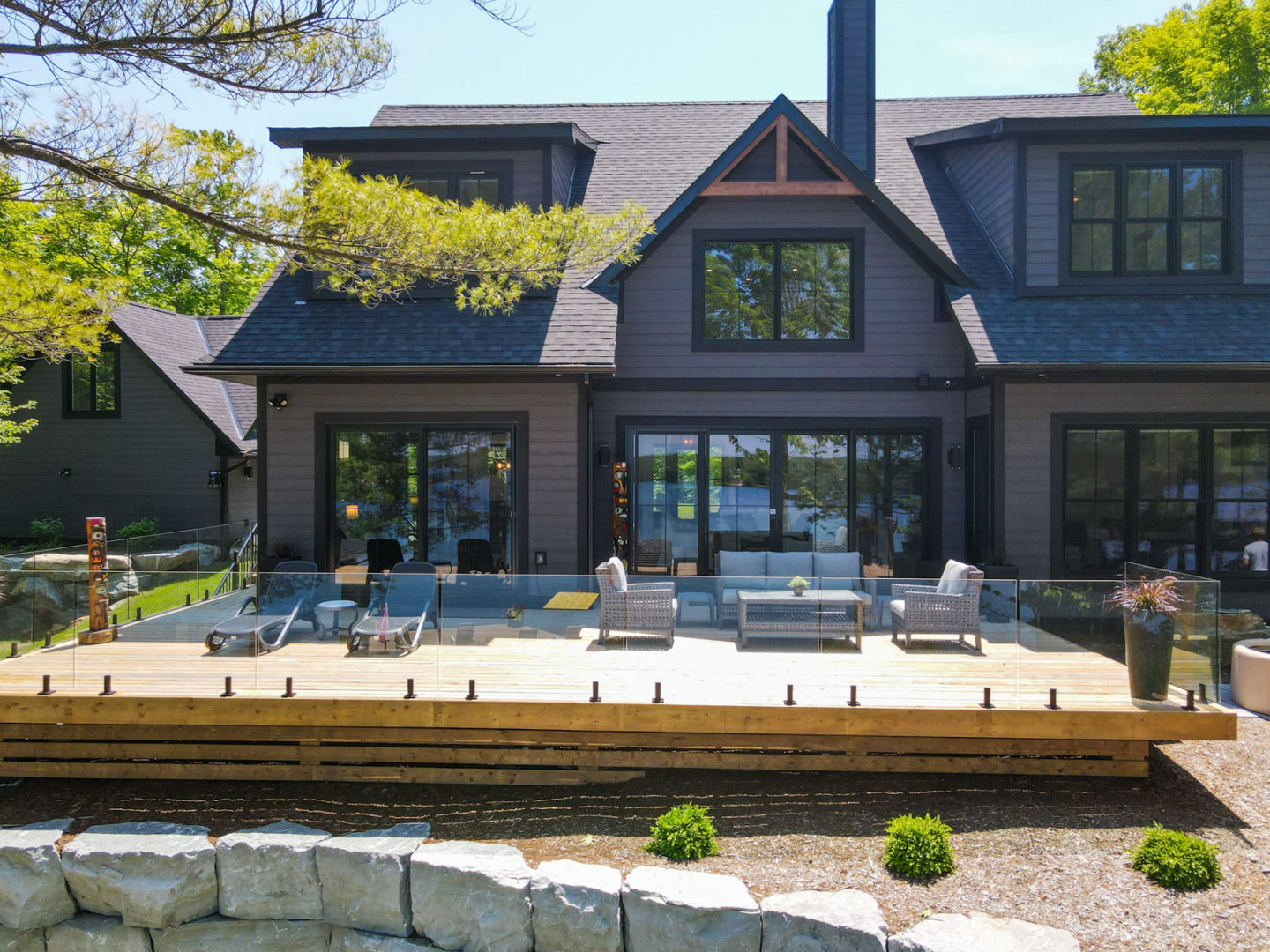 The back of a large, modern cottage with two stories and many wide windows. A large deck with a glass railing branches off the house.