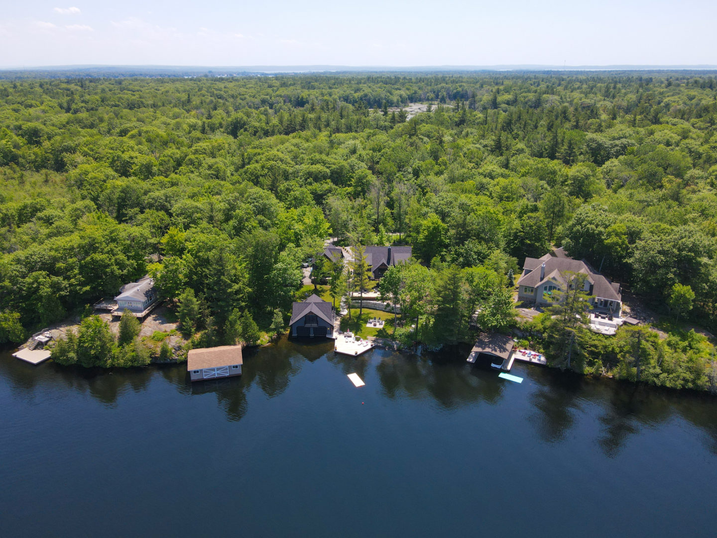 An overhead view of a segment of lakefront, lined with large cottages and dense green trees.