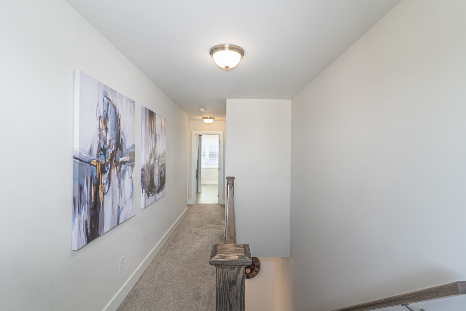 A narrow hallway with carpeted flooring and a wooden railing overlooking a staircase.
