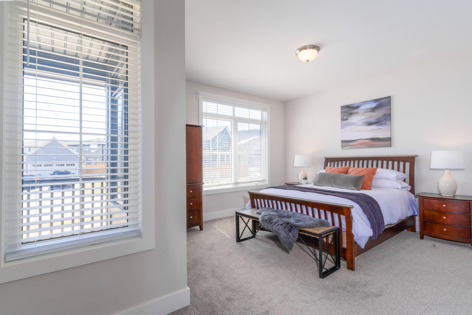 A large, bright bedroom with two windows, a dresser, and a big bed.
