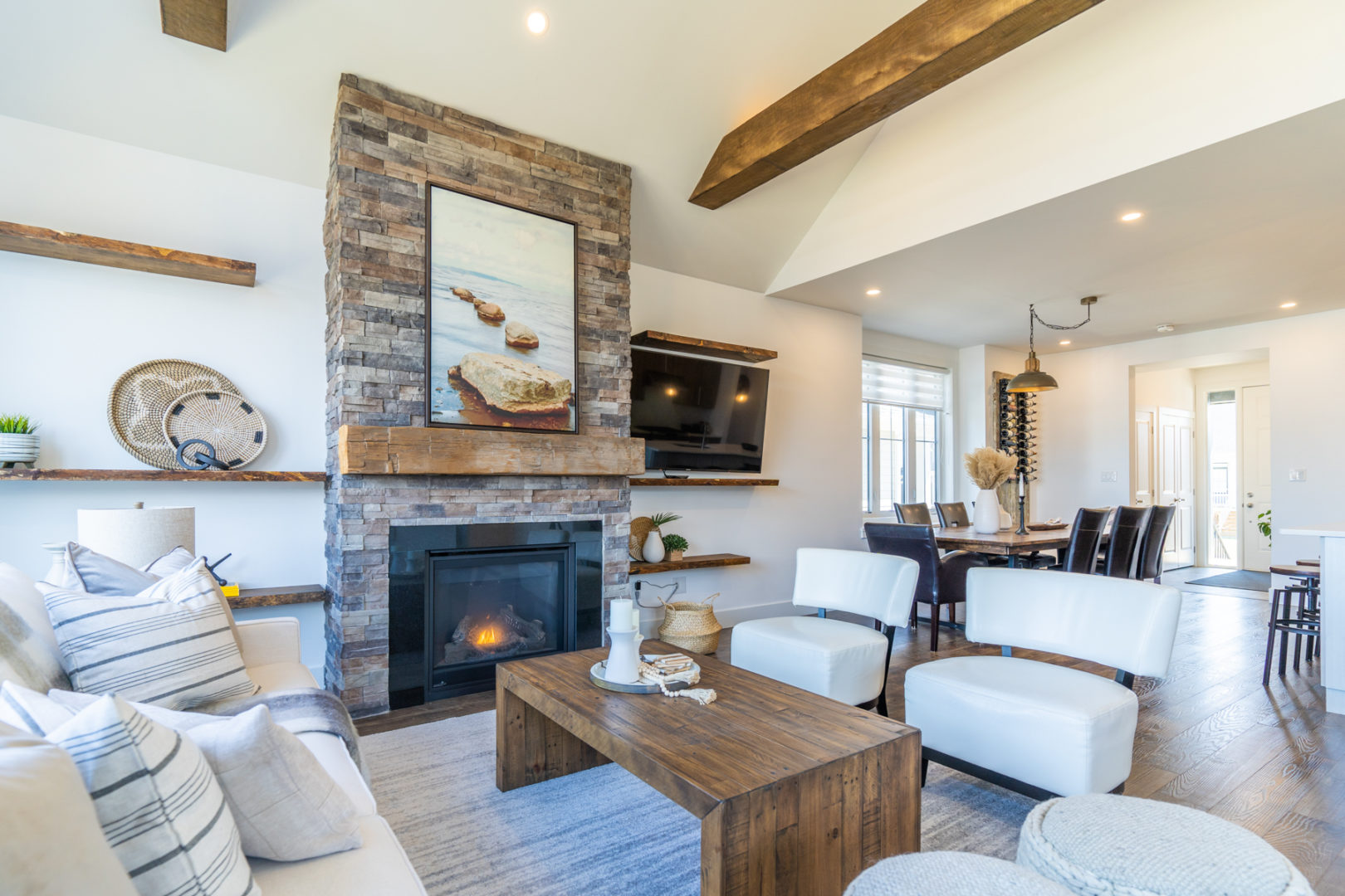 A bright living room with white couches and chairs, a stone fireplace, and a television.