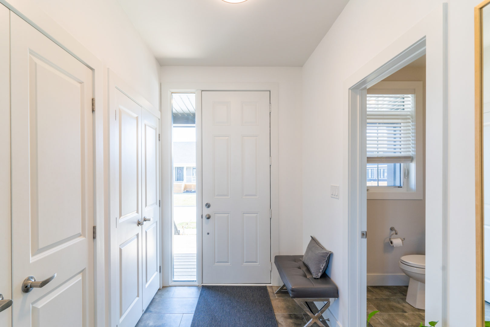 A bright entrance way of a house, with large closets in the wall and a bathroom off to the other side of the front door.